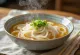 Kake udon osnovna udon juha v skledi z dashi osnovo, okrašena s svežo mlado čebulo in sezamovimi semeni
