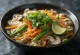 Pho z zelenjavo v skledi, postrežen z riževimi rezanci, zelenjavo, svežim koriandrom in rezinami limete